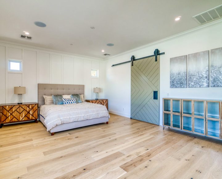 the bedroom that has a sliding barn door, wood flooring, white painted wall and a king size bed on the second story home