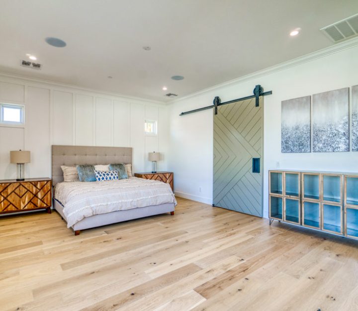 the bedroom that has a sliding barn door, wood flooring, white painted wall and a king size bed on the second story home